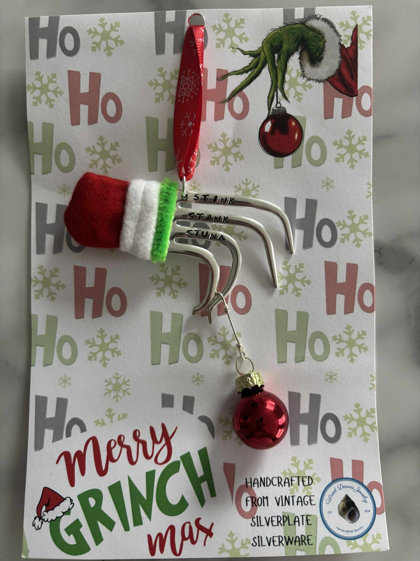 Handmade vintage silverware Christmas Ornament made from a fork shaped as the hand of the Grinch holding a Christmas bauble